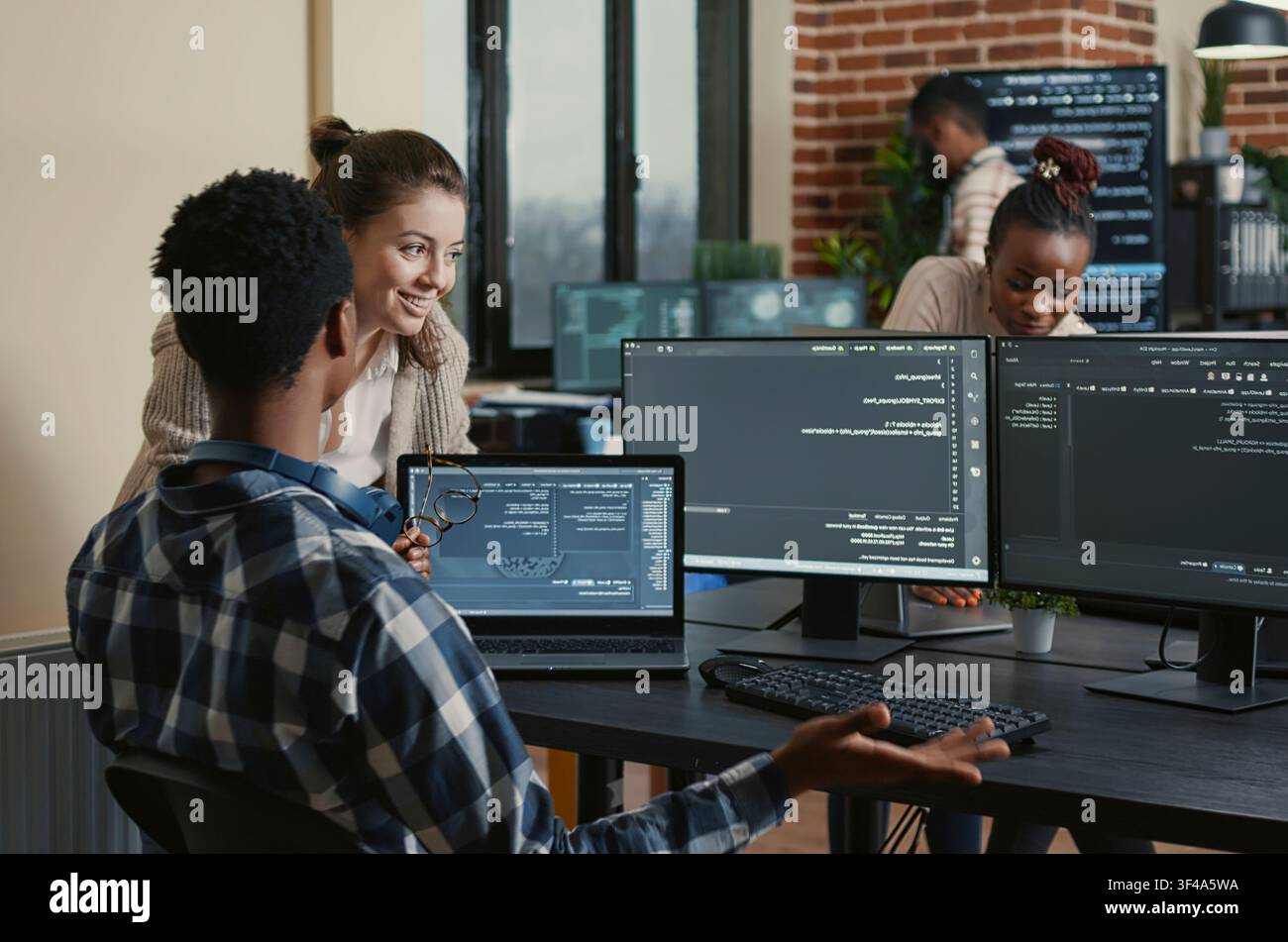Software developers celebrate a successful code compile with a high five at an office desk, surrounded by screens showing programming and algorithms. Stock Photo