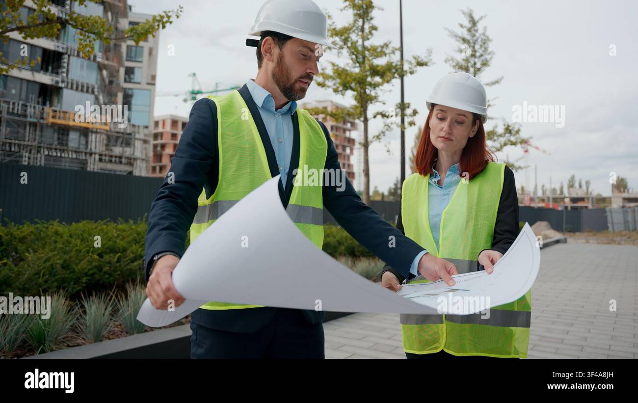 Two contractors civil engineers discuss blueprint city buildings plan project electrical maintenance looking at paper partnership teamwork Stock Photo