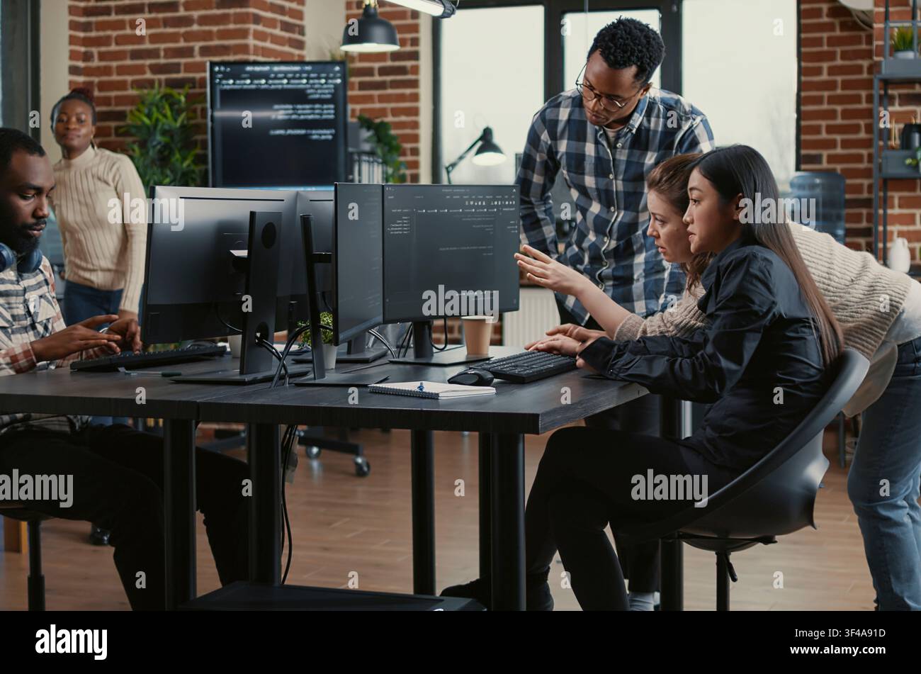 Programmers collaborating on group project compiling algorithm for new cloud computing user interface on computer screens, mixed team of software engineers brainstorming ideas looking at running code. Stock Photo