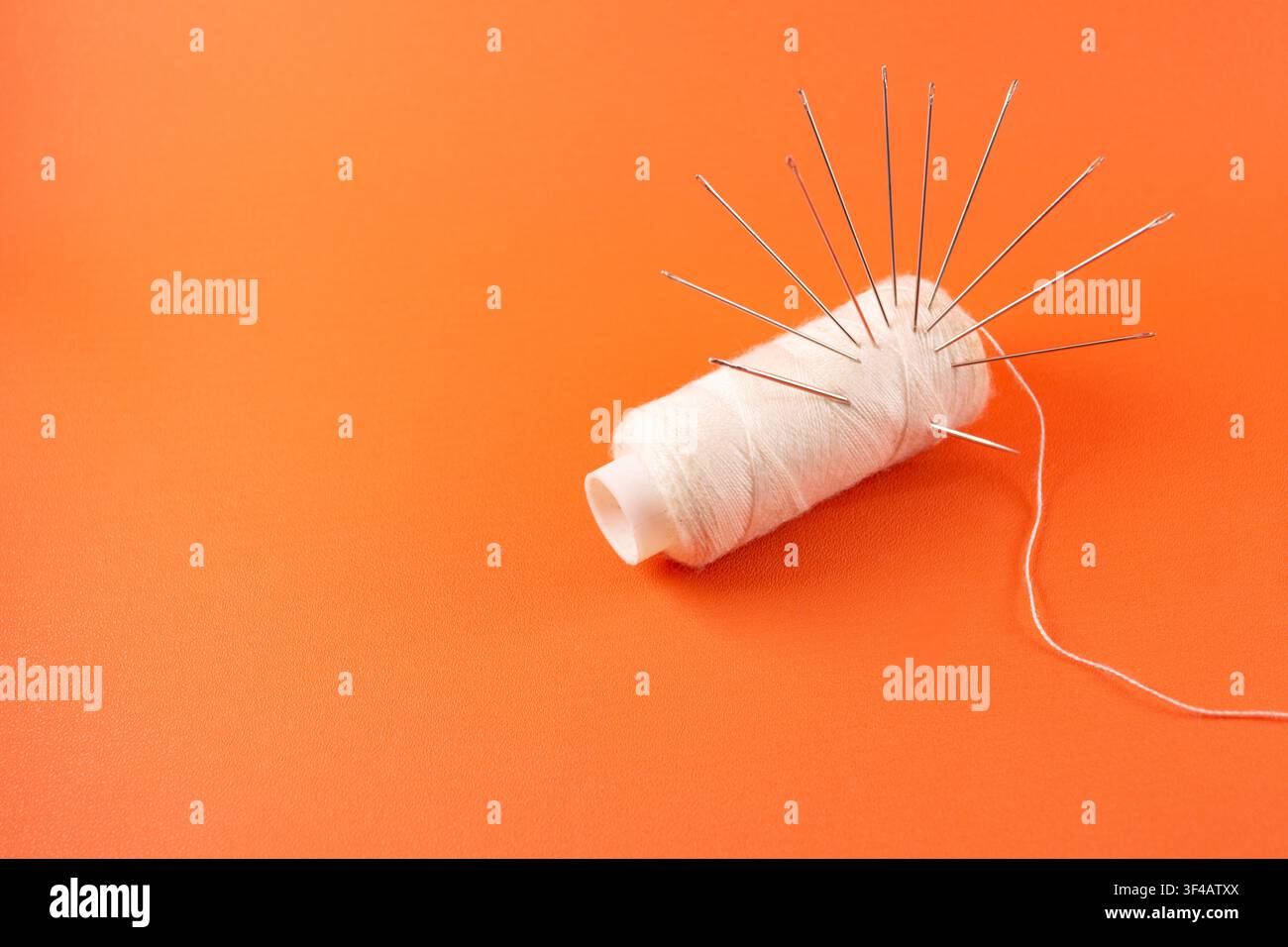 needles and thread isolated orange color background Stock Photo
