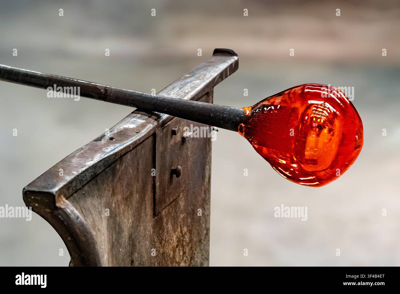 A glowing blob of molten glass gathered at the end of a blowpipe (metal ...