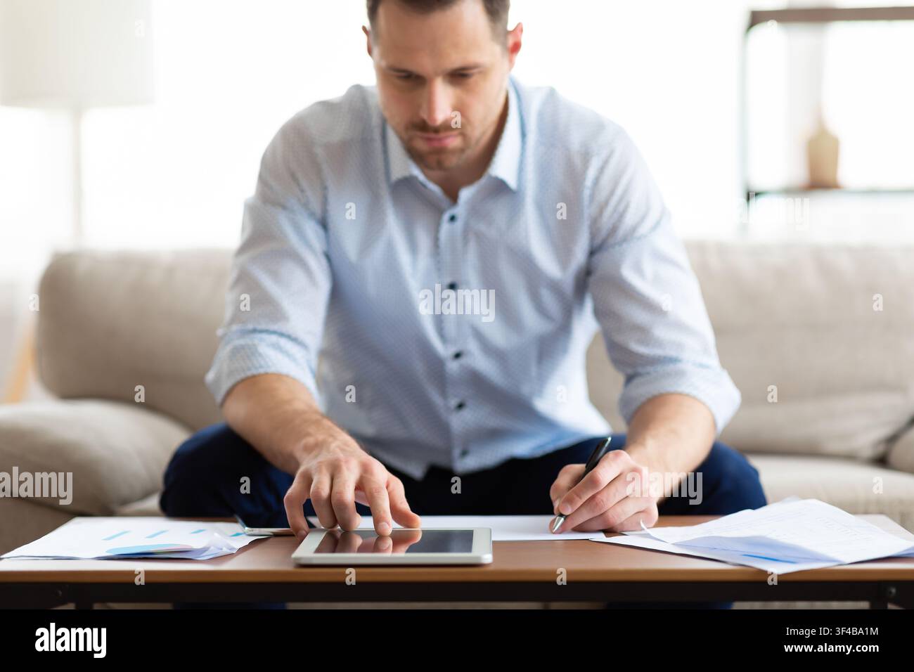 Man using tablet at home and writing notes Stock Photo