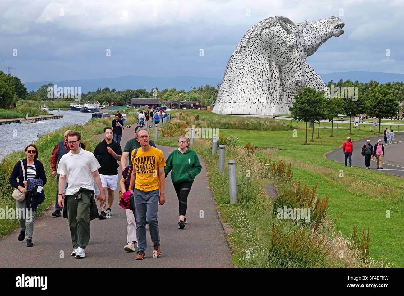 Visitors walk through The Helix park with The Kelpies sculpture in the background, Falkirk, Scotland, UK. Stock Photo