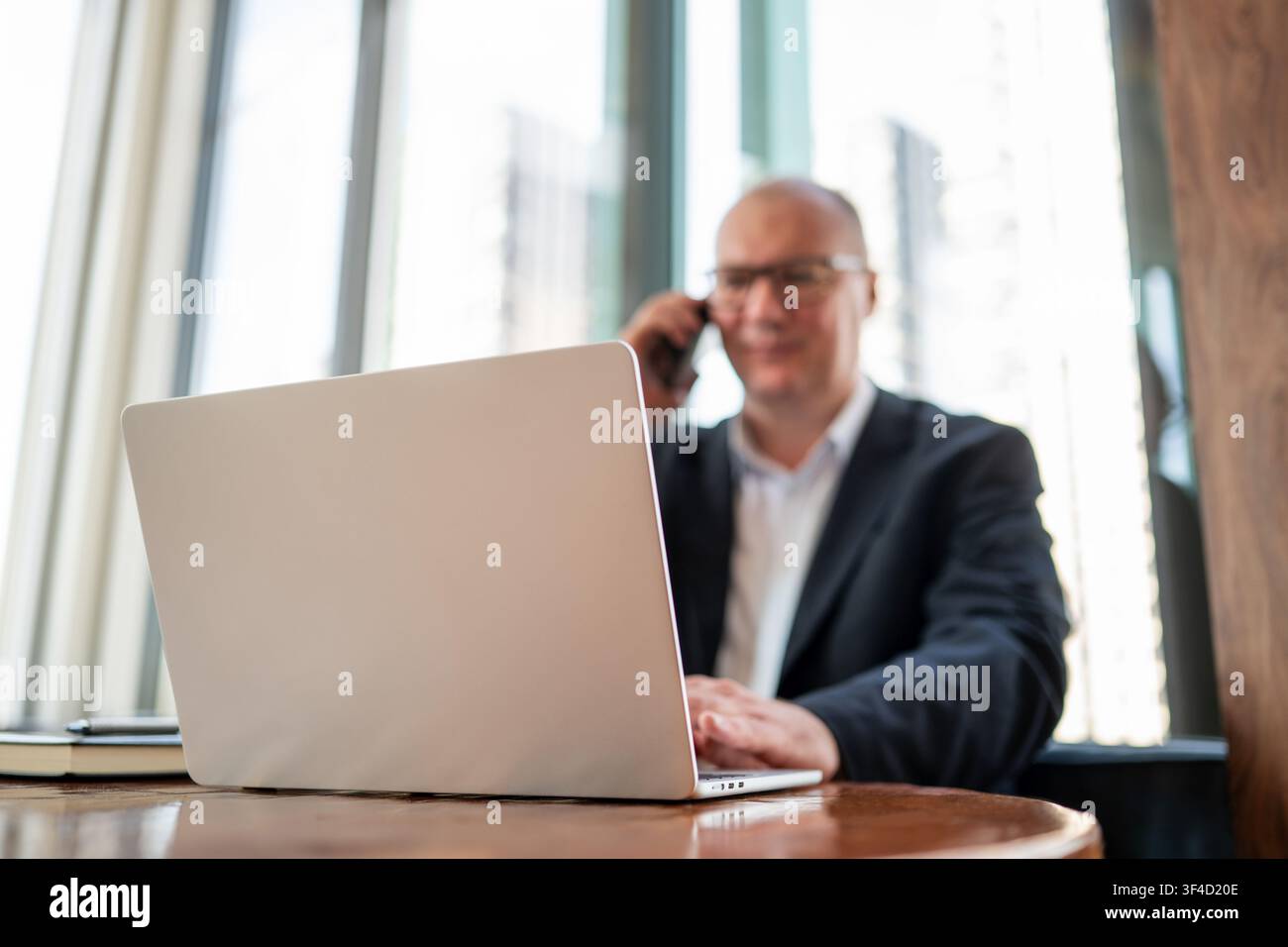 Businessman talking on smartphone while working on laptop in cafe Stock Photo