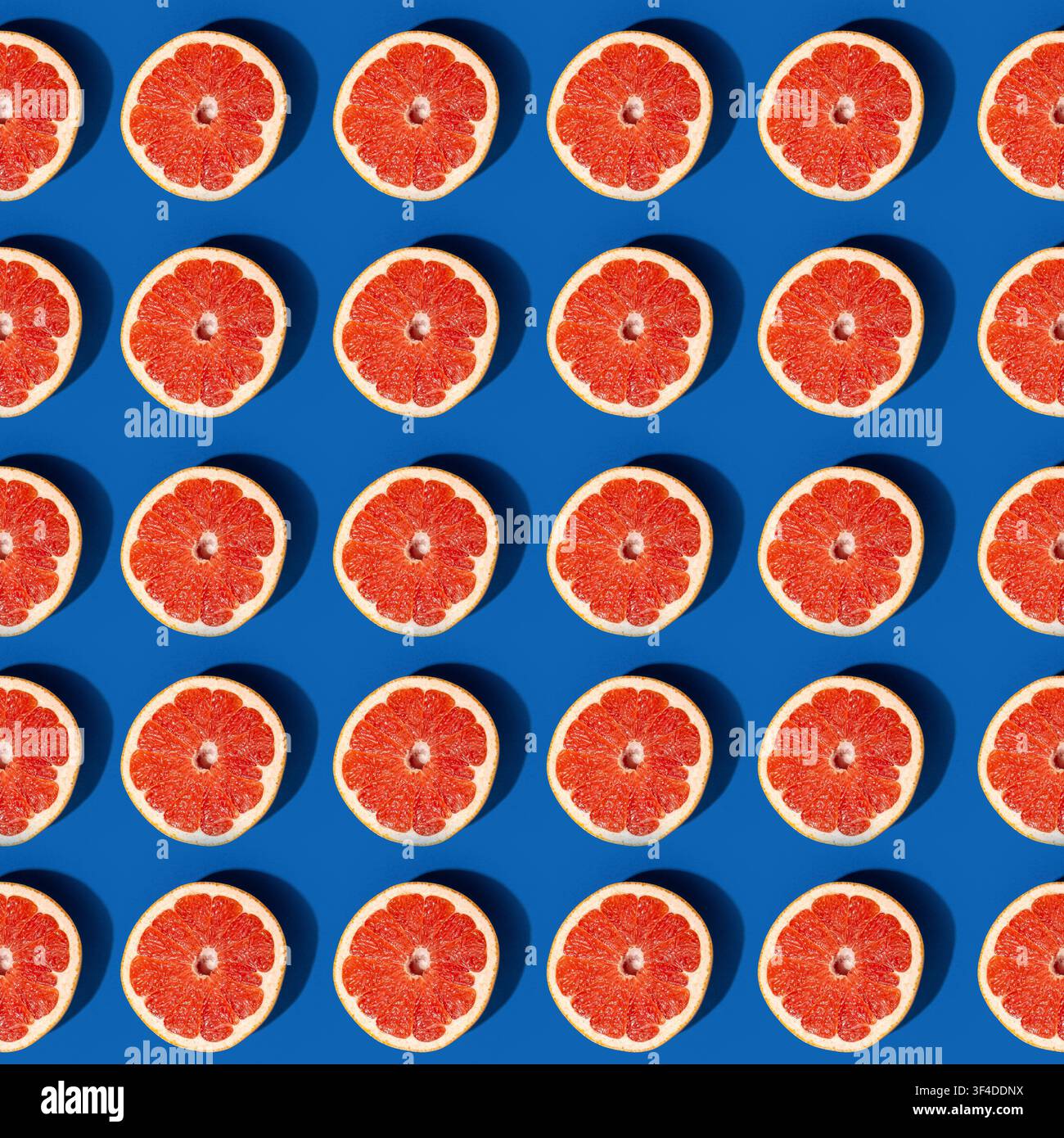 Grapefruit halves arranged in geometric pattern on dark blue background Stock Photo