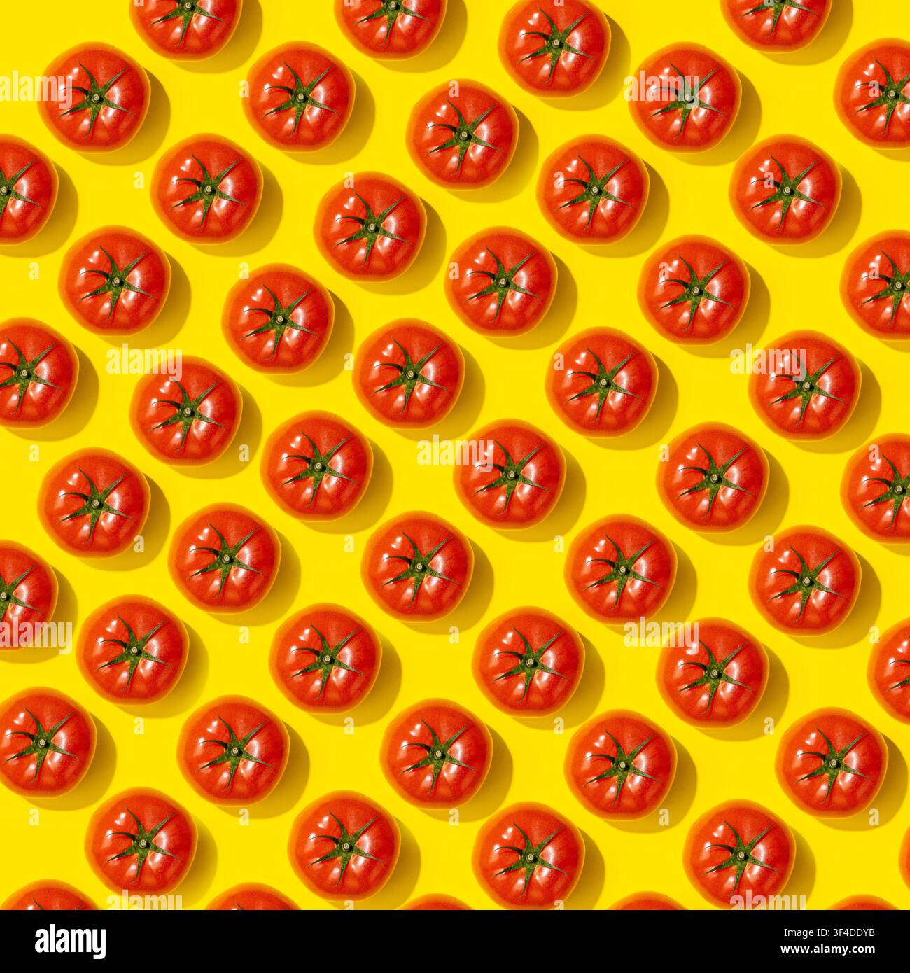 Whole red tomatoes arranged in dense pattern on bright yellow background Stock Photo