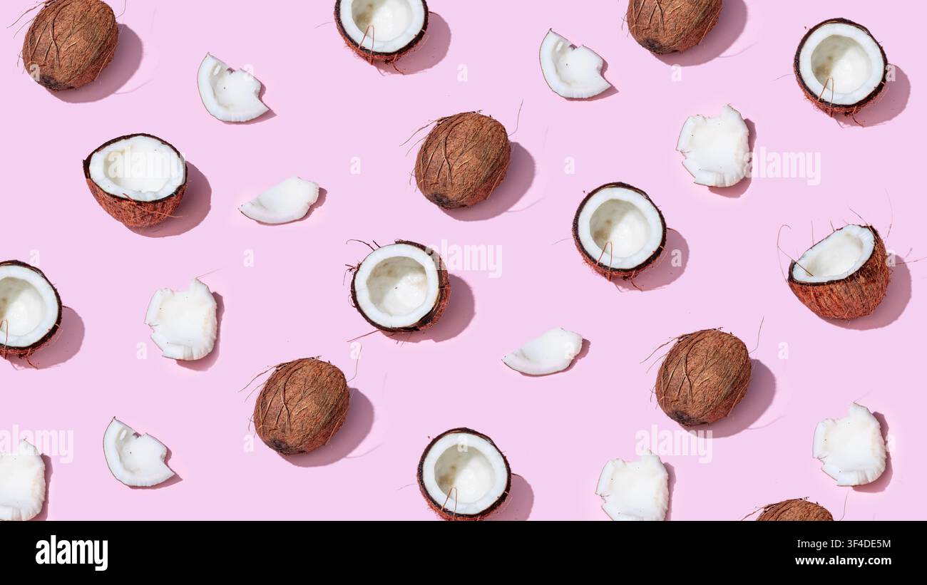 Whole and halved coconuts arranged in pattern on pastel pink background Stock Photo