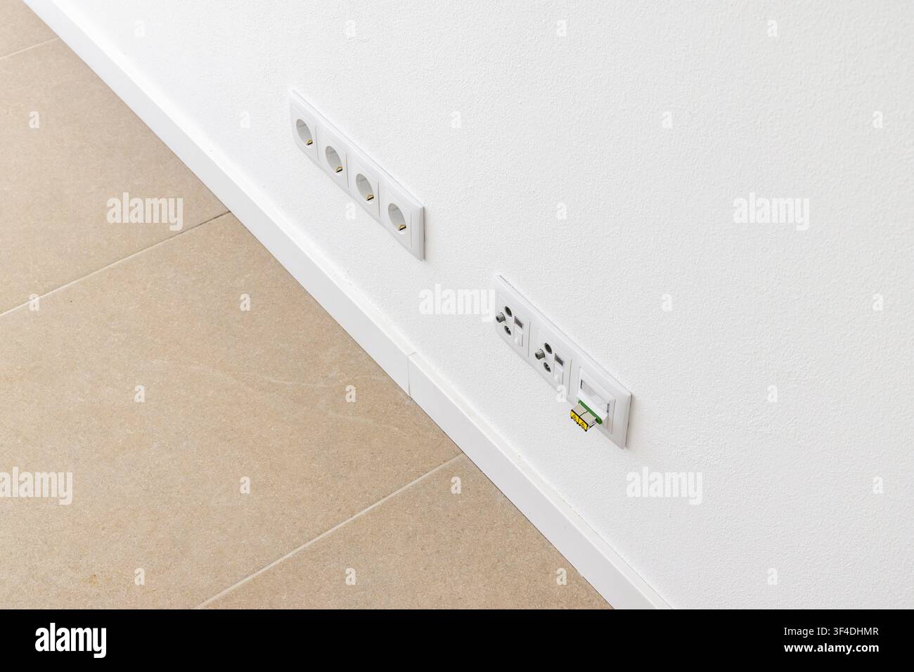 A clean white wall features multiple electrical sockets and a network data port with a yellow connector inserted Stock Photo