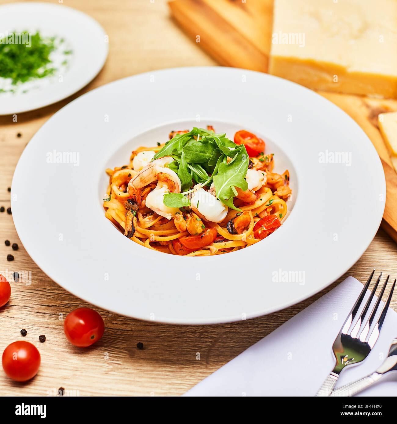 Seafood pasta with shrimps, mussels, cherry tomatoes and fresh arugula in a white plate on a wooden table with parmesan and parsley. Stock Photo