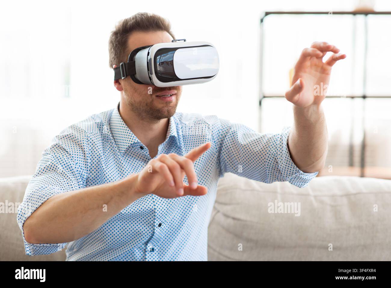 Young guy wearing virtual reality glasses, sitting on sofa Stock Photo