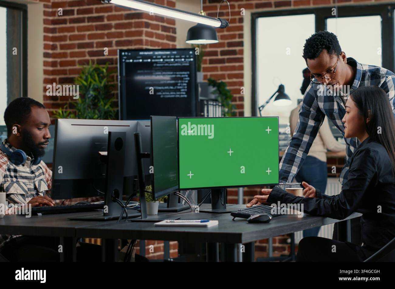 Developers analyze source code with green screen while colleagues work on algorithms and a chroma key mockup supports replaceable software screen use. Stock Photo