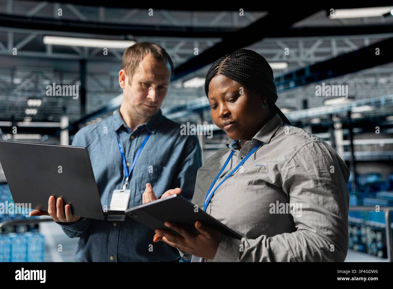 Team of data center system administrators scanning equipment for errors using devices. Server farm colleagues working together, backing up supercomputers data using software on laptop Stock Photo