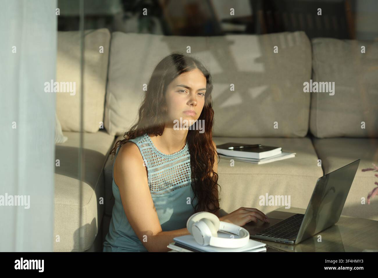 Pensive and distracted serious student looking through a window at home Stock Photo