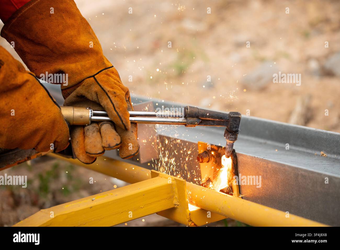 Bright sparks flying while worker cuts metal beam with torch on construction site Stock Photo