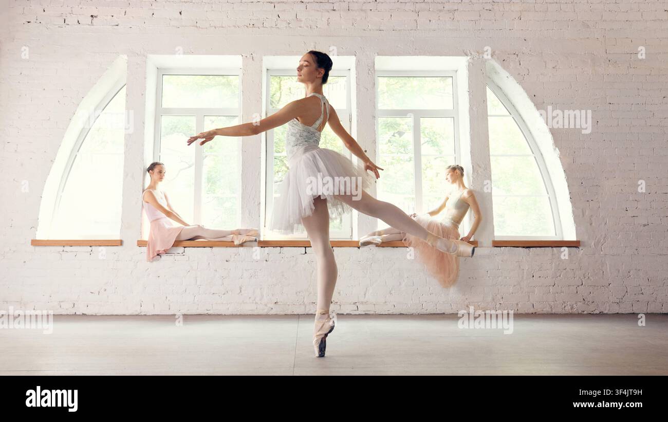 Ballet dancer balancing in foreground while group rests near windows Stock Photo