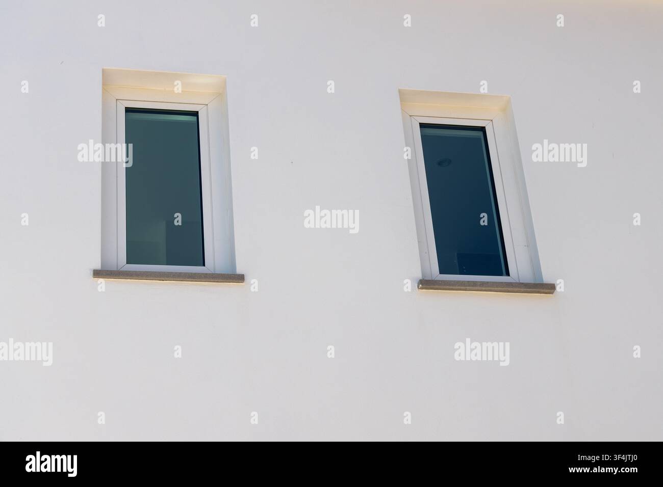 A close-up view shows two rectangular windows with dark glass set into a rough white stucco facade Stock Photo