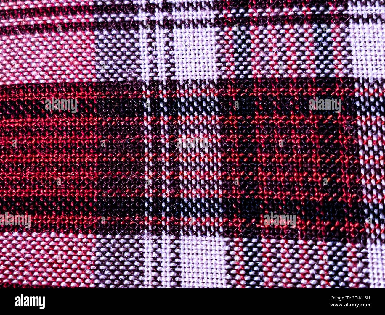 Macro shot of a woven plaid fabric featuring a traditional checkered pattern in red, black, and white threads. Stock Photo