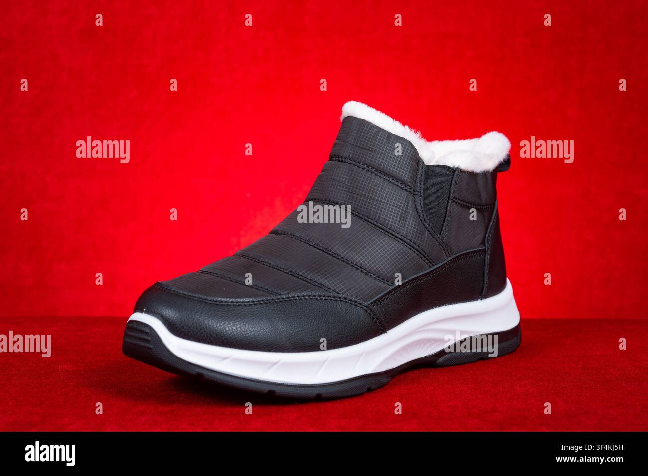 Fleece lined black winter ankle boot against red background Stock Photo