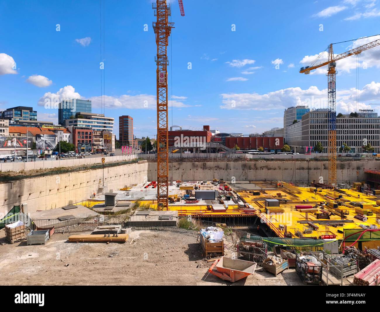 A large urban construction site foundation pit with tall yellow cranes and modern city buildings under a blue sky, focusing on industrial growth. - Smartphone Captured Stock Image