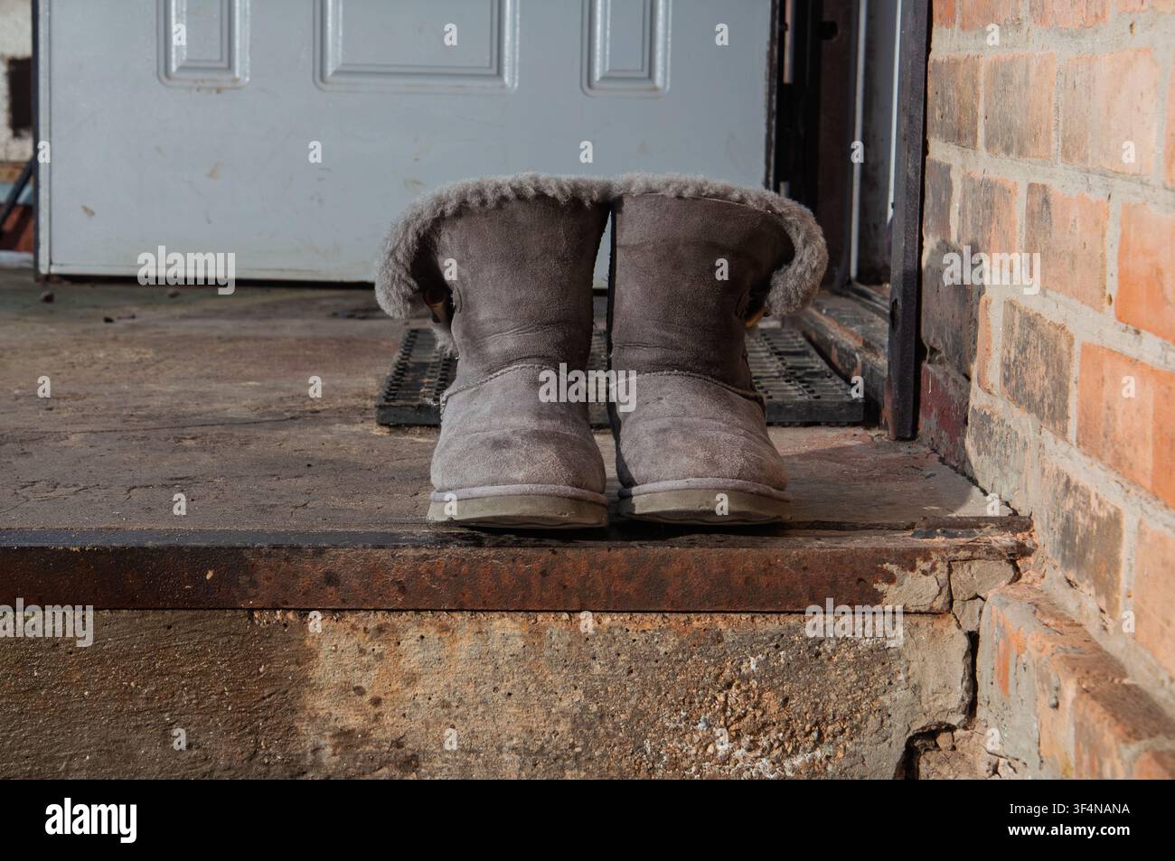 Cozy sheepskin boots left outside on a weathered doorstep near a brick wall Stock Photo