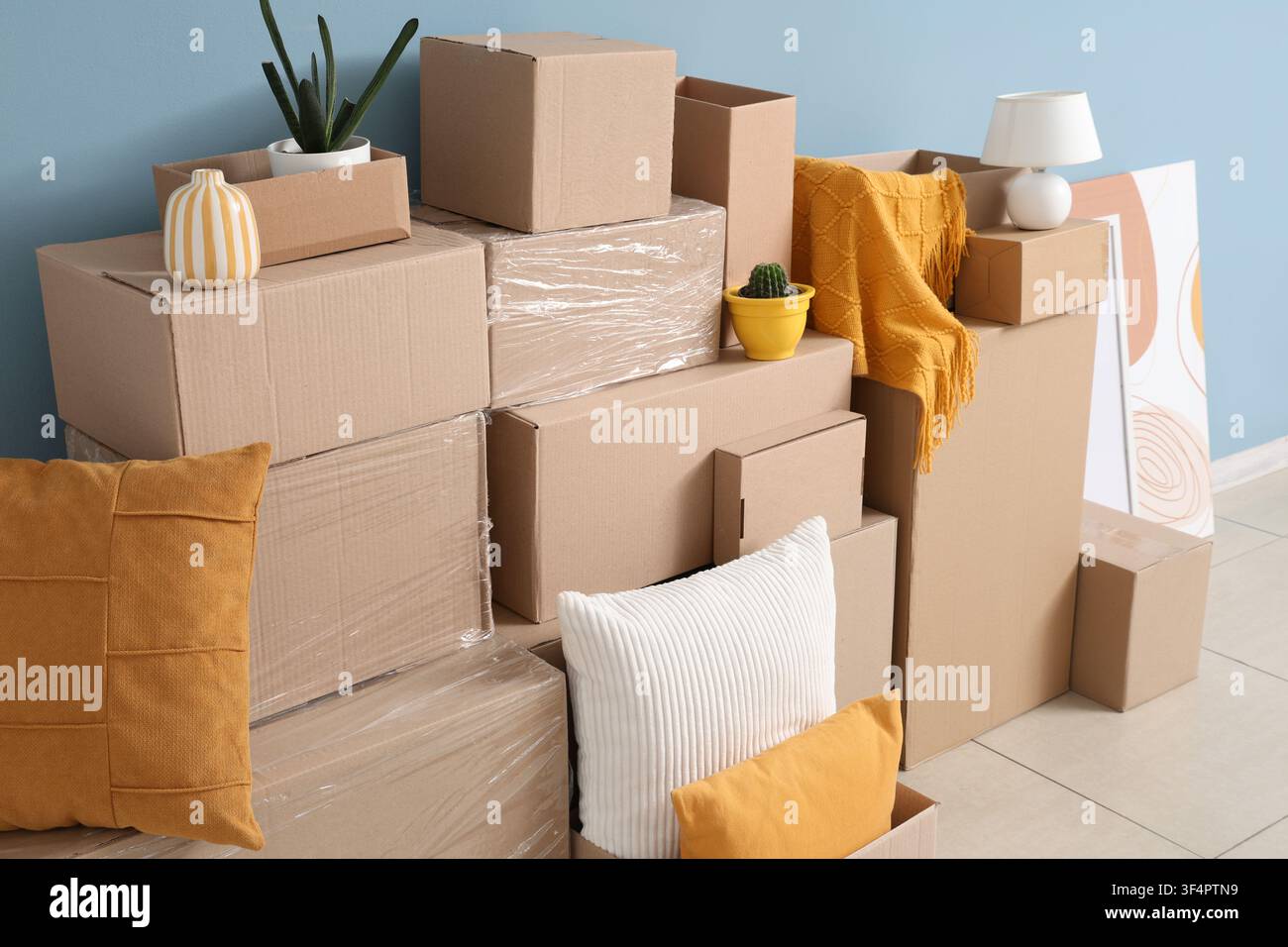 Stacked cardboard boxes and household items for moving or relocation against a blue wall, new home Stock Photo