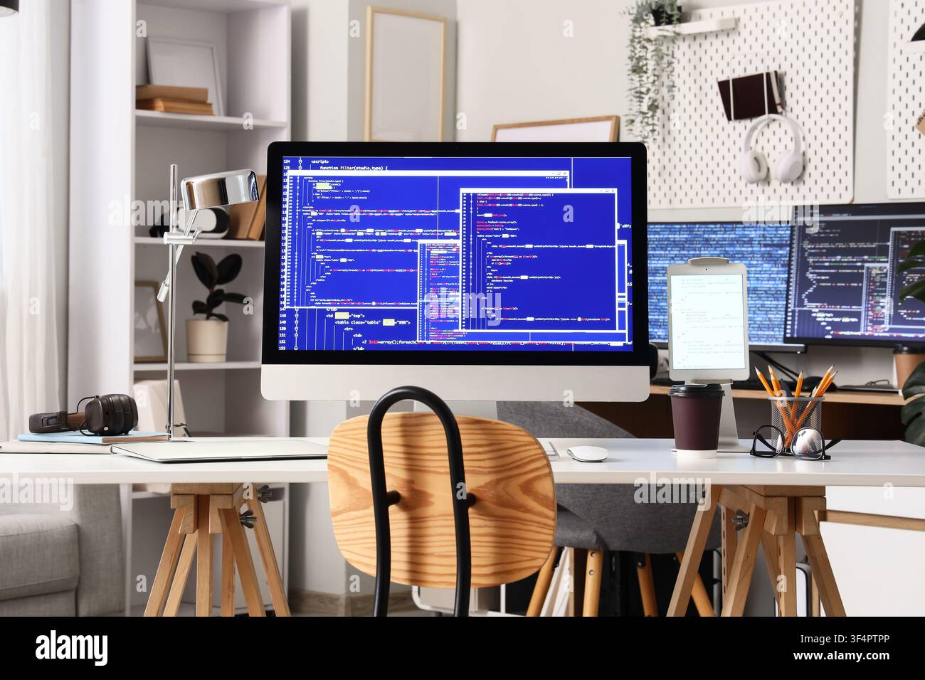 Modern home office workspace with multiple computer screens displaying programming code and development software development Stock Photo