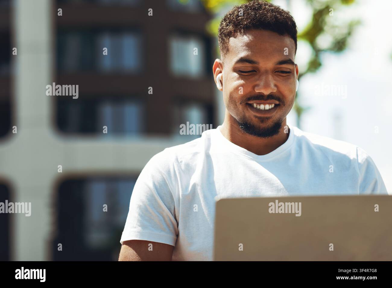 Smiling Young Black Man Working On Laptop Outdoors, Focused On Task, Business Concept Stock Photo