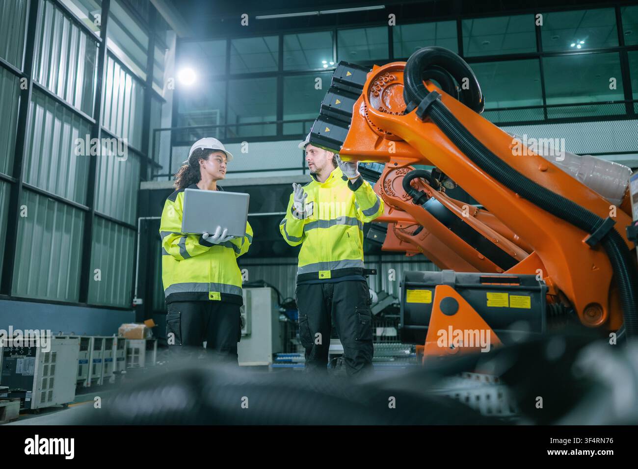Industrial engineers inspects orange robotic arm automated machinery in warehouse factories. Concept industrial maintenance service, equipment quality Stock Photo
