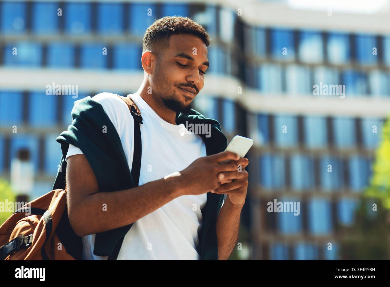 Young African American Man Using Smartphone Outdoors, Relaxed Posture, Urban Setting Stock Photo