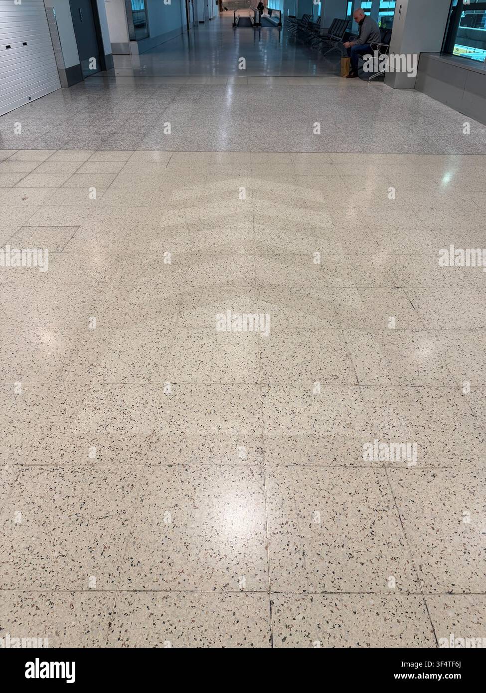 A polished terrazzo floor stretches toward a lone traveller seated in an airport terminal. - Smartphone Captured Stock Image