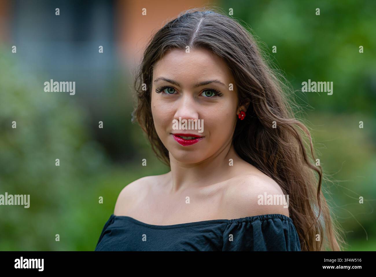 A woman with long hair and red lips poses confidently in an outdoor area. Stock Photo