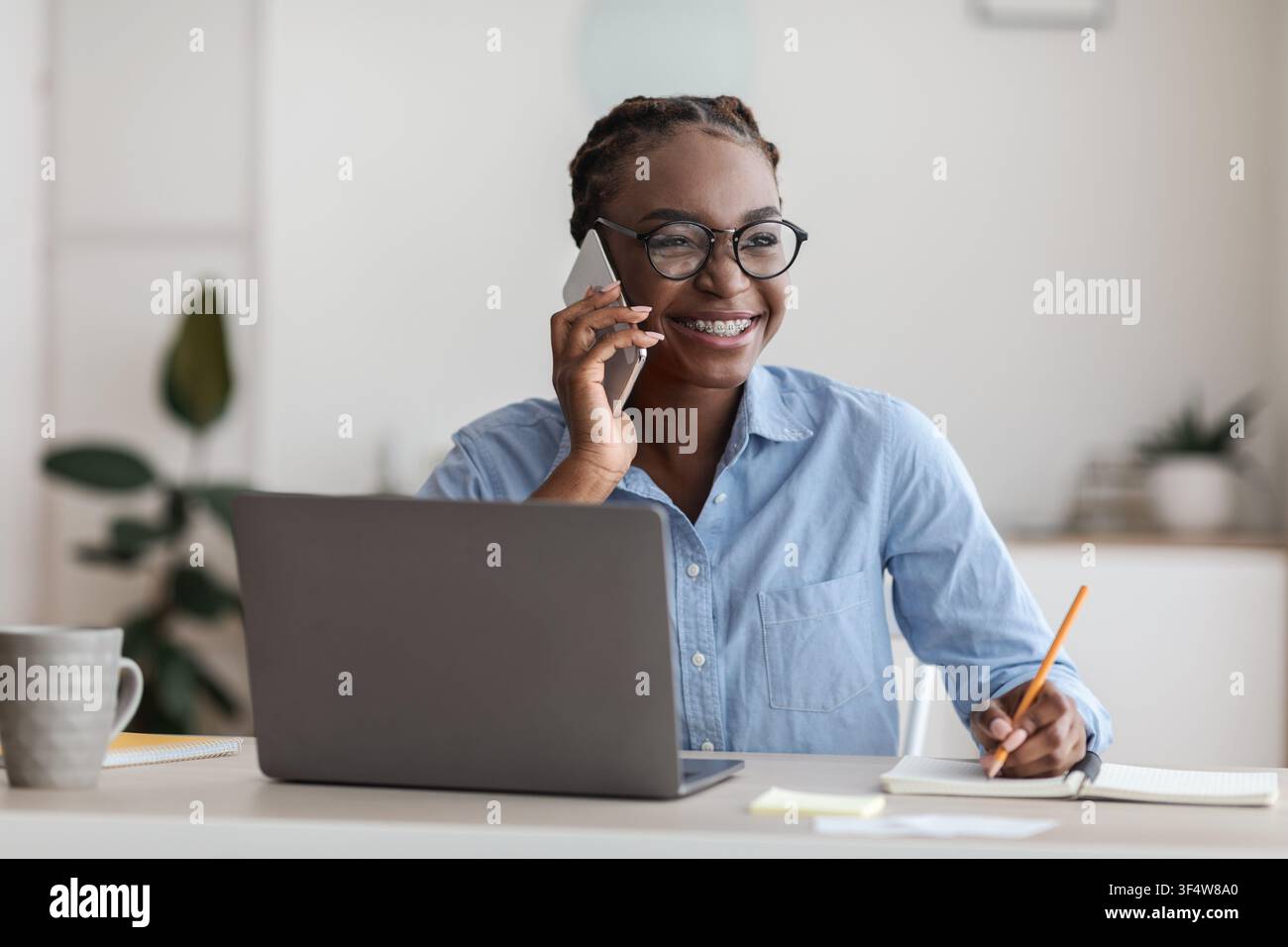 Black Female Office Manager Talking On Cellphone And Taking Notes At Workplace Stock Photo