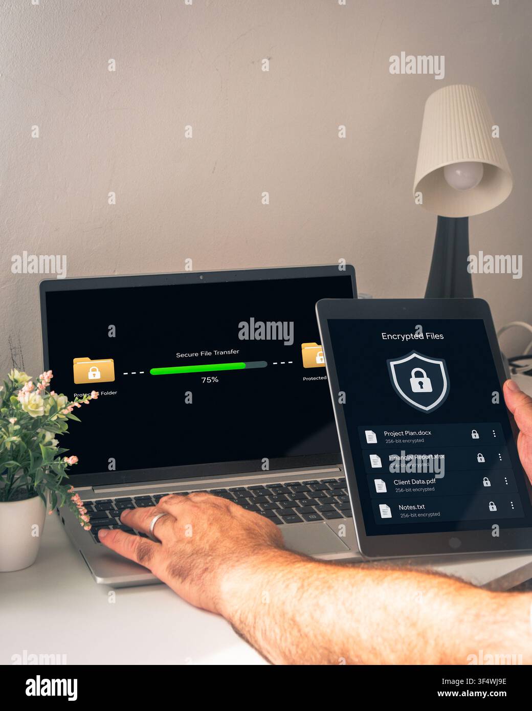 Hands use a laptop beside a tablet showing encrypted files while a secure file transfer progresses between protected folders on screen. Stock Photo