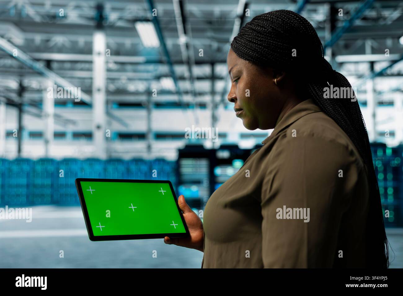 Data center admin monitors components for potential failures using green screen tablet, improving system stability. Server hub worker uses chroma key device to configure settings, increases uptime Stock Photo