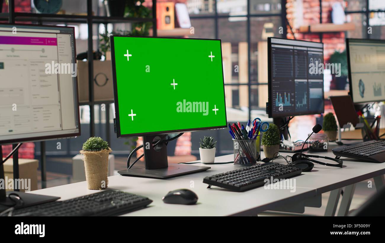 Chroma key computer displays in empty office showing analytics dashboards and data graphs. Office workspace with green screen PCs showing digital data visualization, panning shot Stock Photo