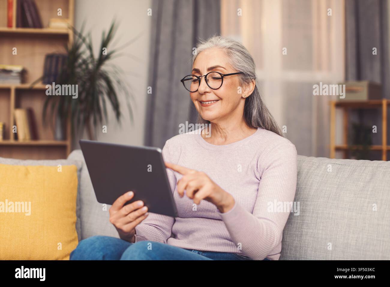 Smiling Elderly Woman Using Tablet At Home, Enjoying Technology And Connection Stock Photo