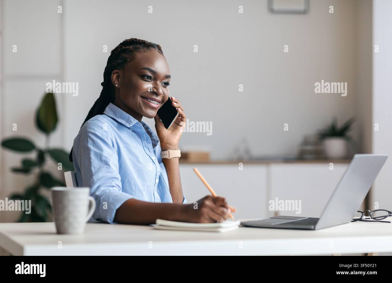Millennial Black Woman Manager Taking Notes And Talking On Cellphone In Office Stock Photo