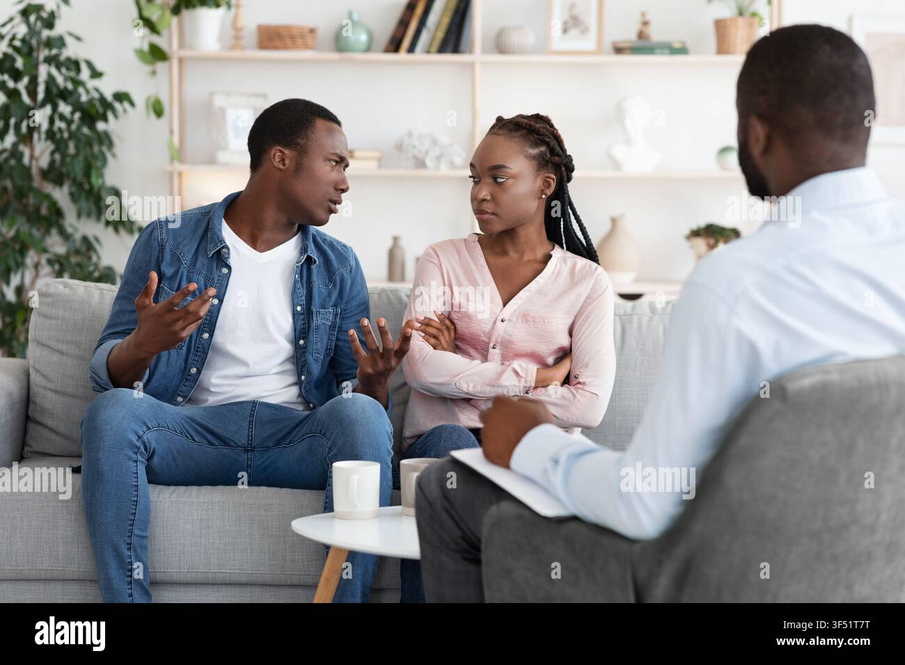 Young Black Spouses Having Relationship Problems, Sitting At Therapy Session With Counselor Stock Photo