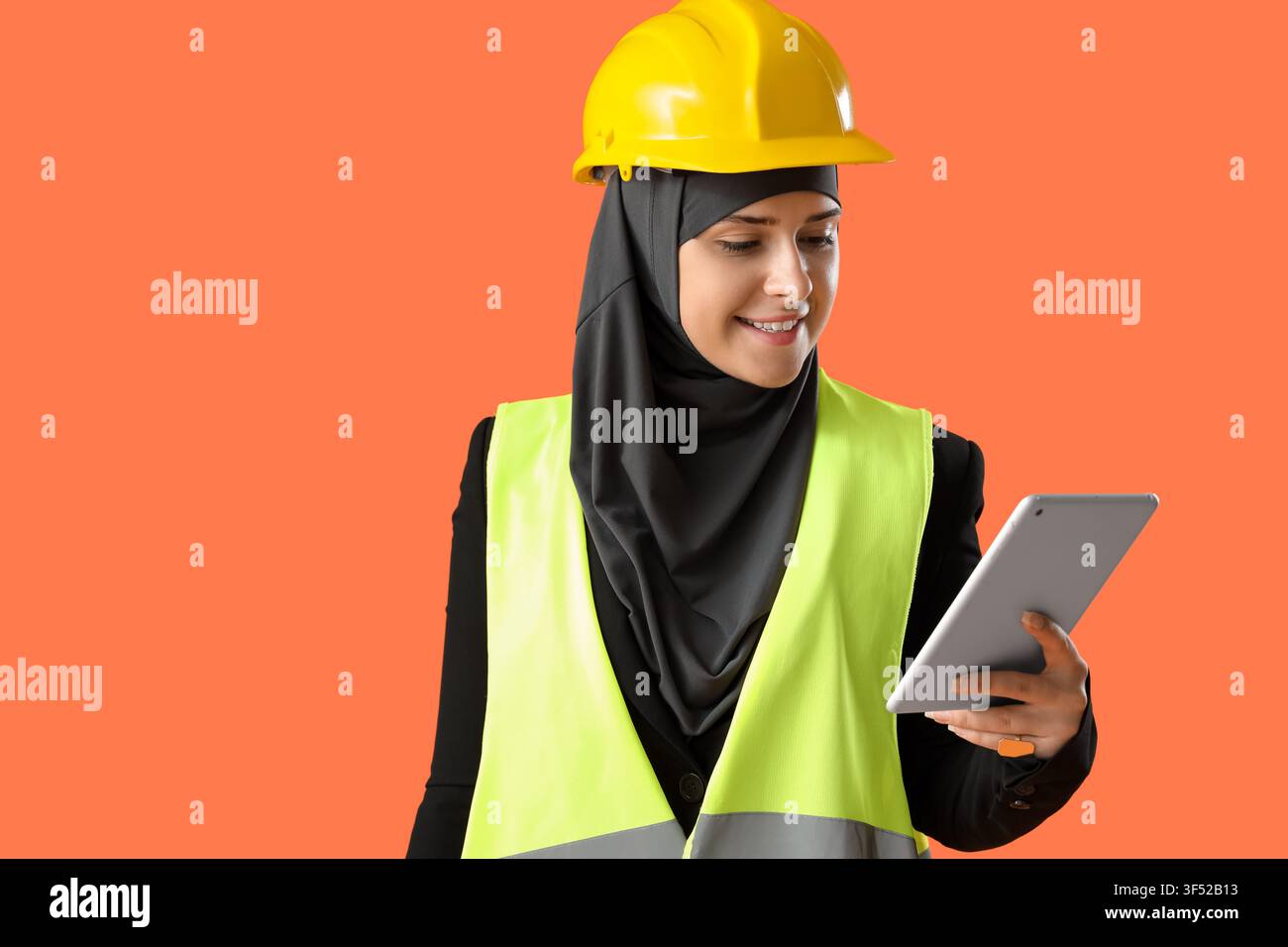 Female Muslim construction worker with tablet computer on orange background Stock Photo