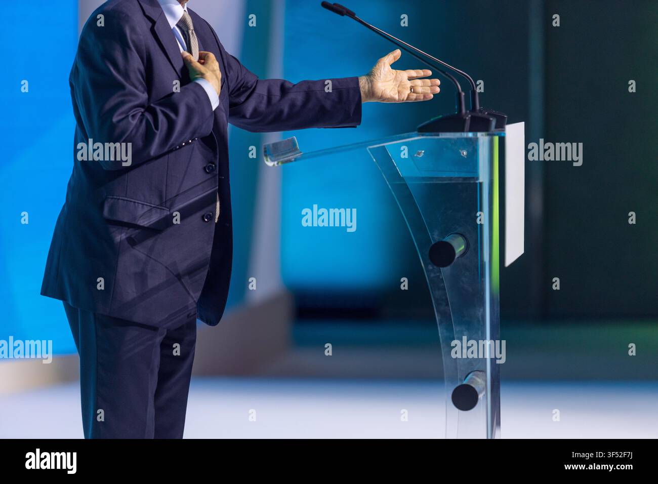 Business executive speaking at conference podium, gesturing during keynote presentation with microphones on stage. Ideal for leadership, communication Stock Photo