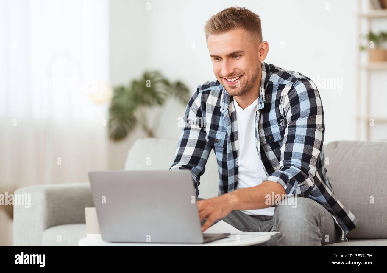 Happy man using laptop sitting on couch Stock Photo