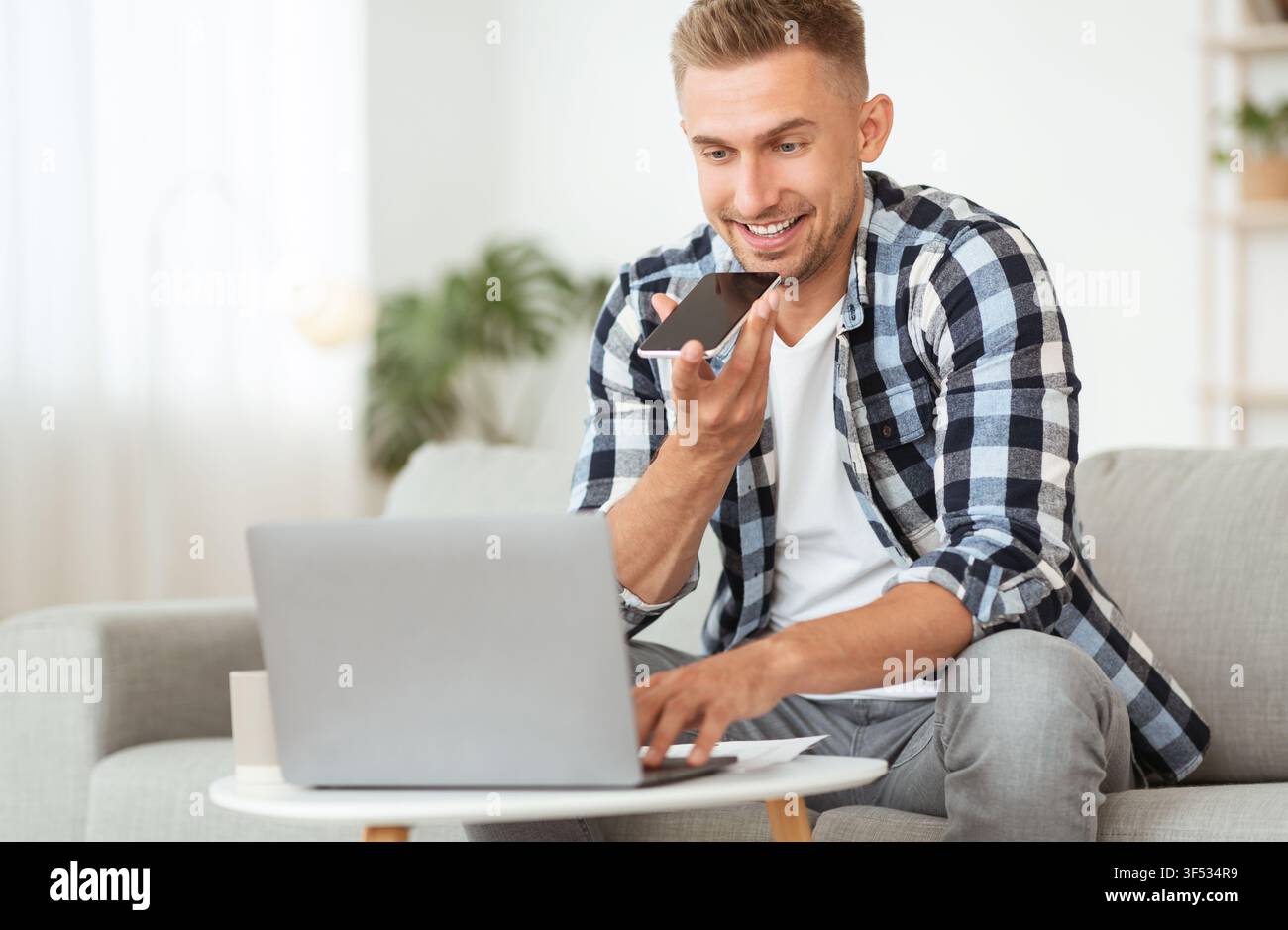 Young man using voice assistant on his cellphone, using pc Stock Photo