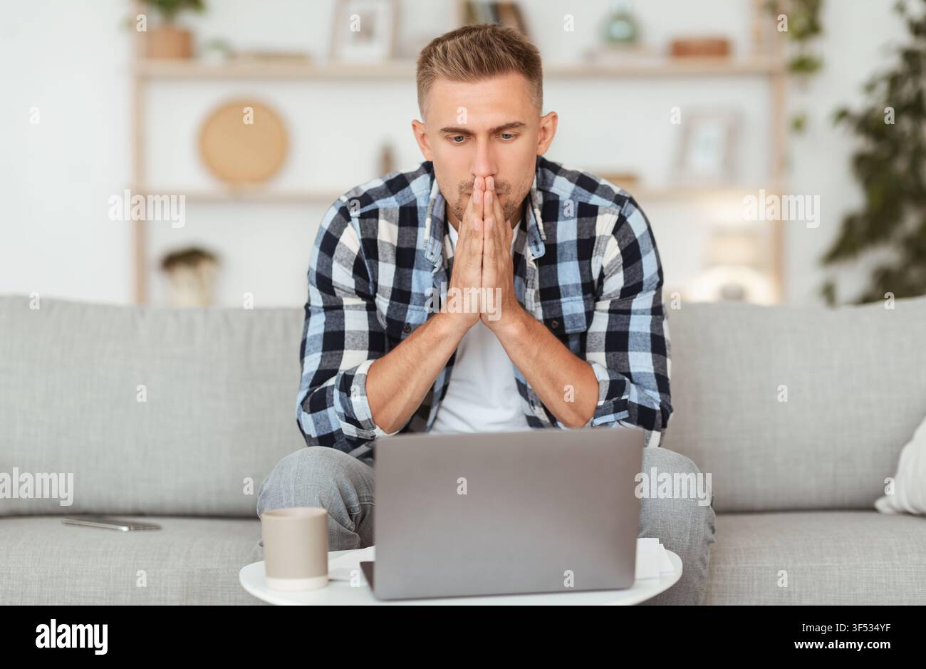 Pensive young man sitting at table, using computer Stock Photo