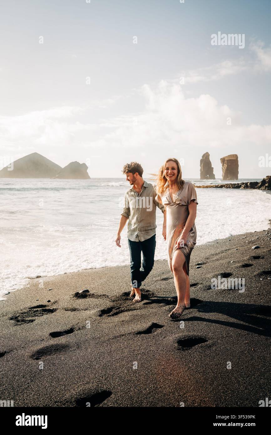 Happy couple enjoys a walk on a black sand beach Stock Photo