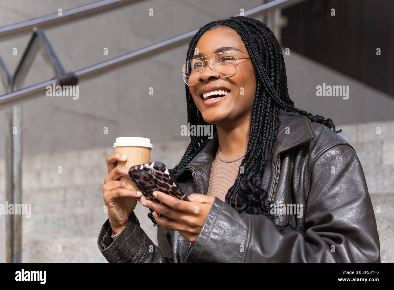 Smiling young woman using smartphone and drinking coffee outdoors Stock Photo