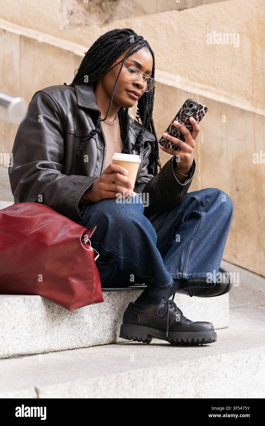 Young student using smartphone and drinking coffee on university steps Stock Photo