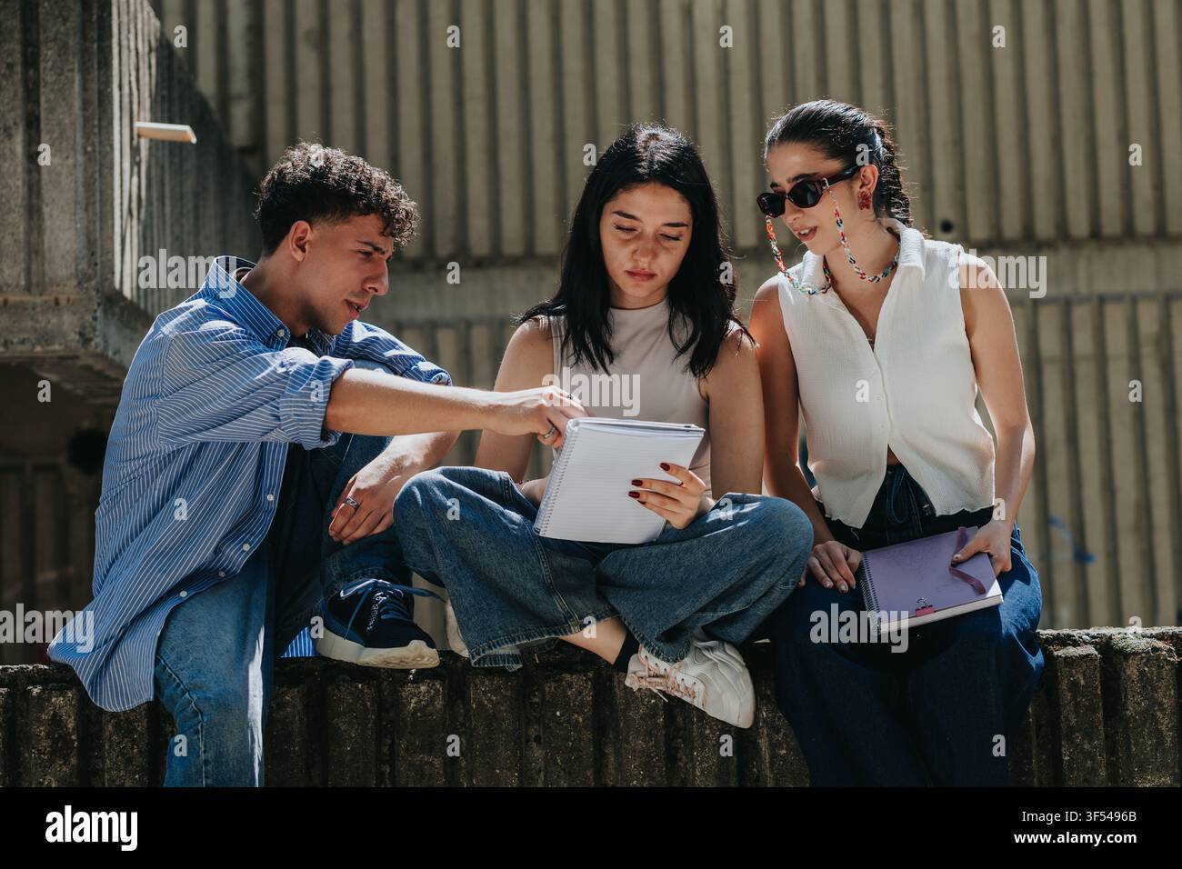 Three students studying together outdoors on campus reviewing notes and discussing coursework Stock Photo