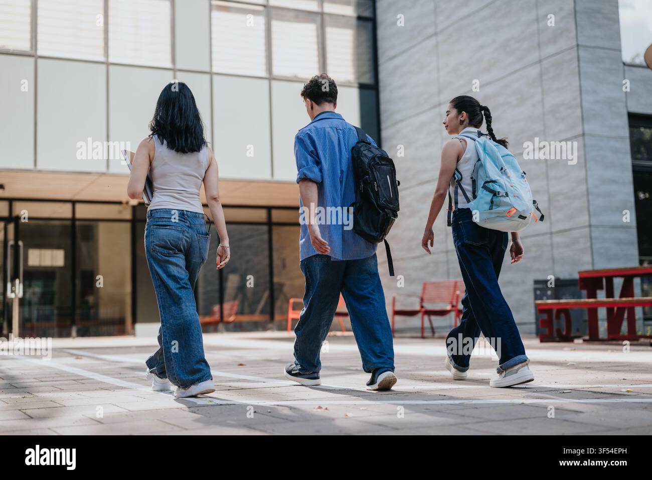 Three students walking on campus courtyard with backpacks and casual clothing Stock Photo