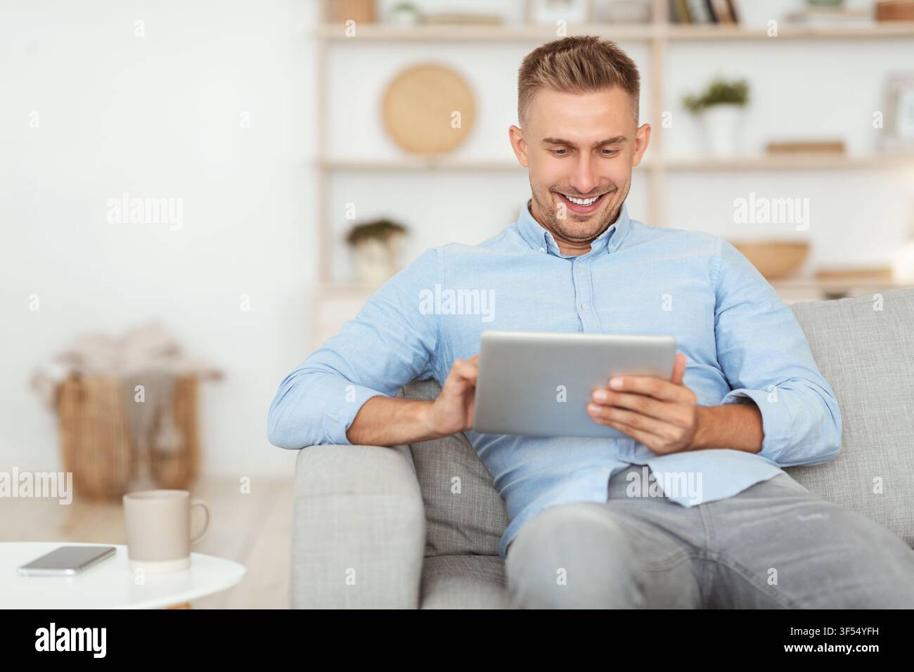 Happy man using digital tablet sitting on sofa Stock Photo