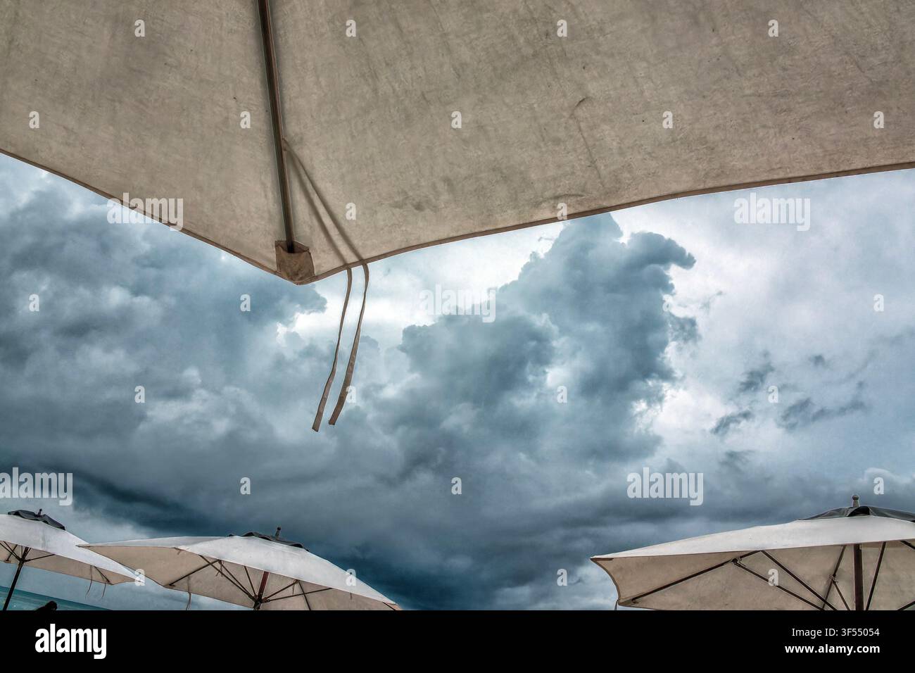 White beach umbrellas set against a dramatic, stormy sky. Stock Photo